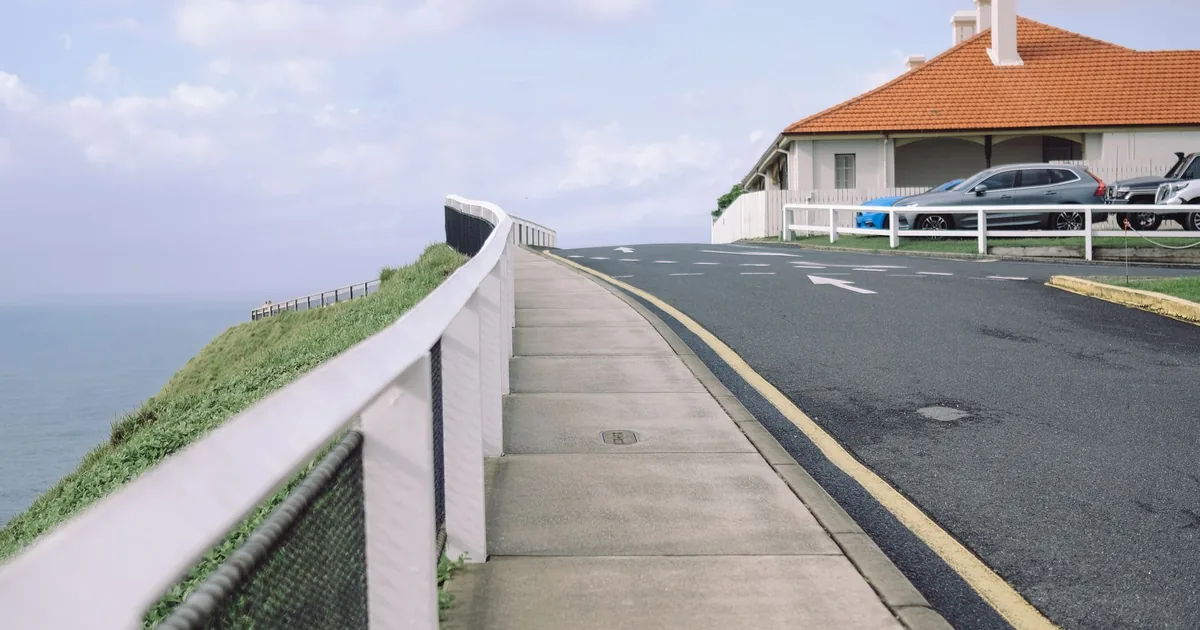 Parking area near a coastal road with a house and several parked.