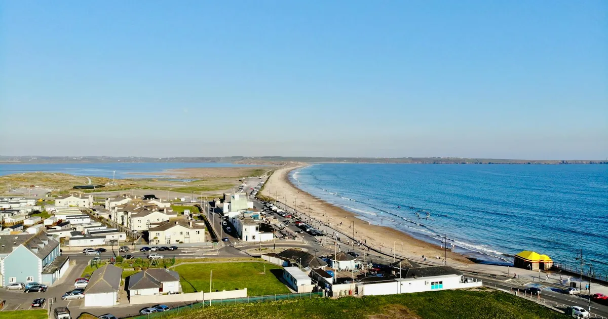 Parking area near the beach with cars and a view of the coastline.