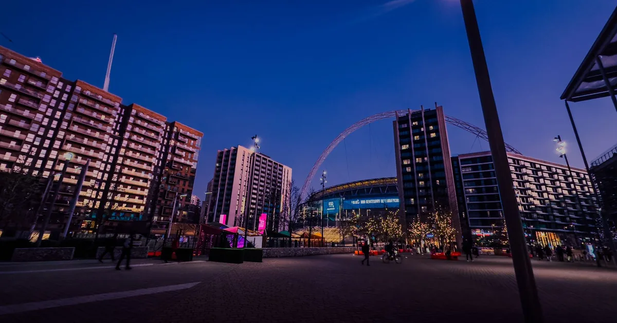 Parking area with buildings and a stadium in the background at dusk.