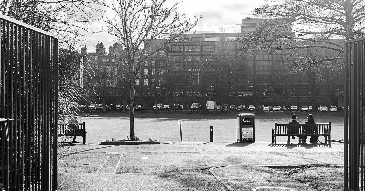 Parking area with multiple cars and two people sitting on a bench.
