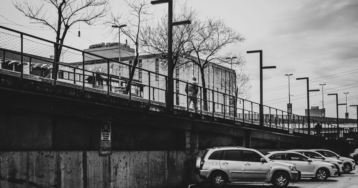 Parking area with several cars and a person walking on an elevated.
