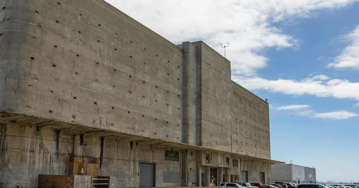 Parking area with several cars next to a large concrete building.