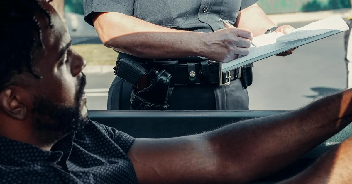 Parking enforcement officer writing a ticket near a parked vehicle.