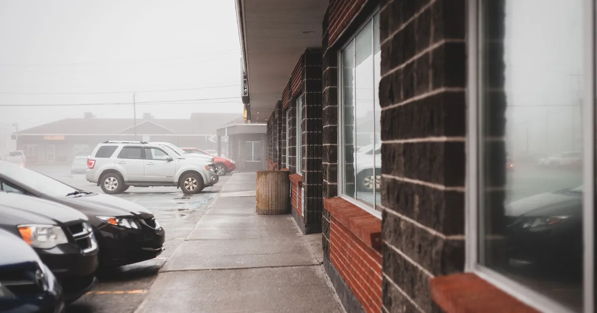 Parking lot with several cars and a building in foggy conditions.