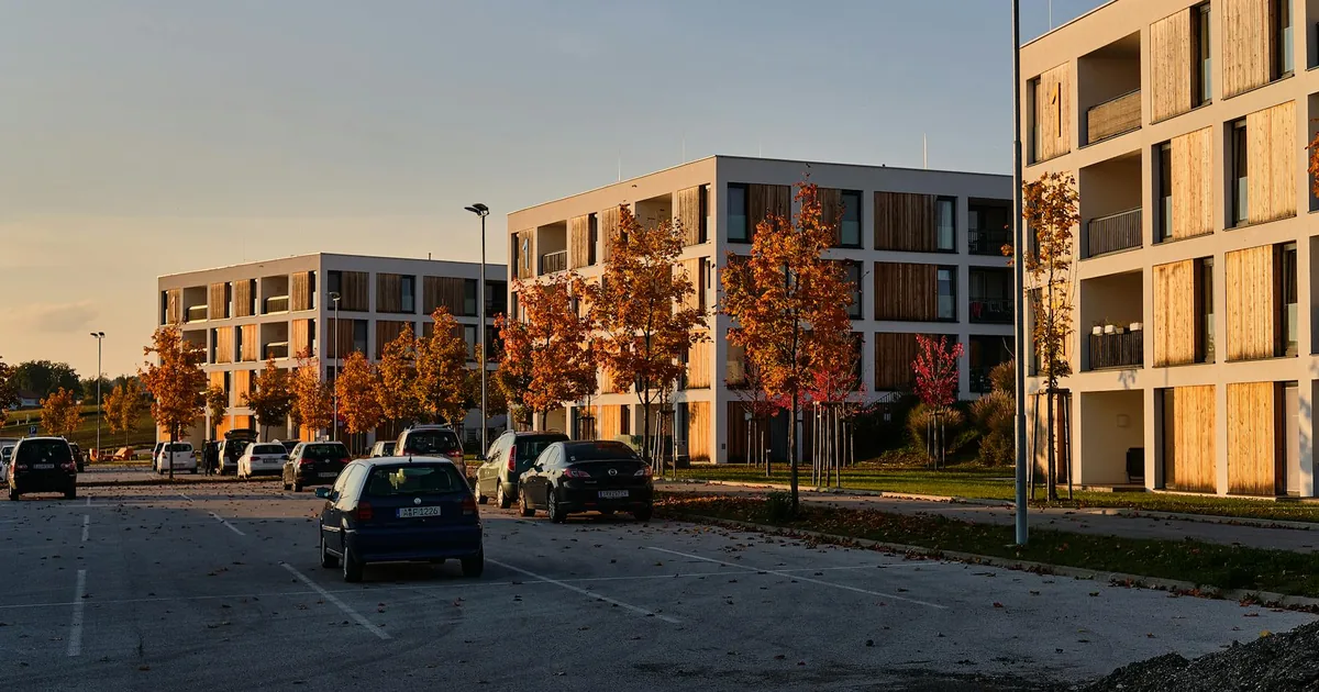 Parking lot with several cars and autumn trees near modern buildings.