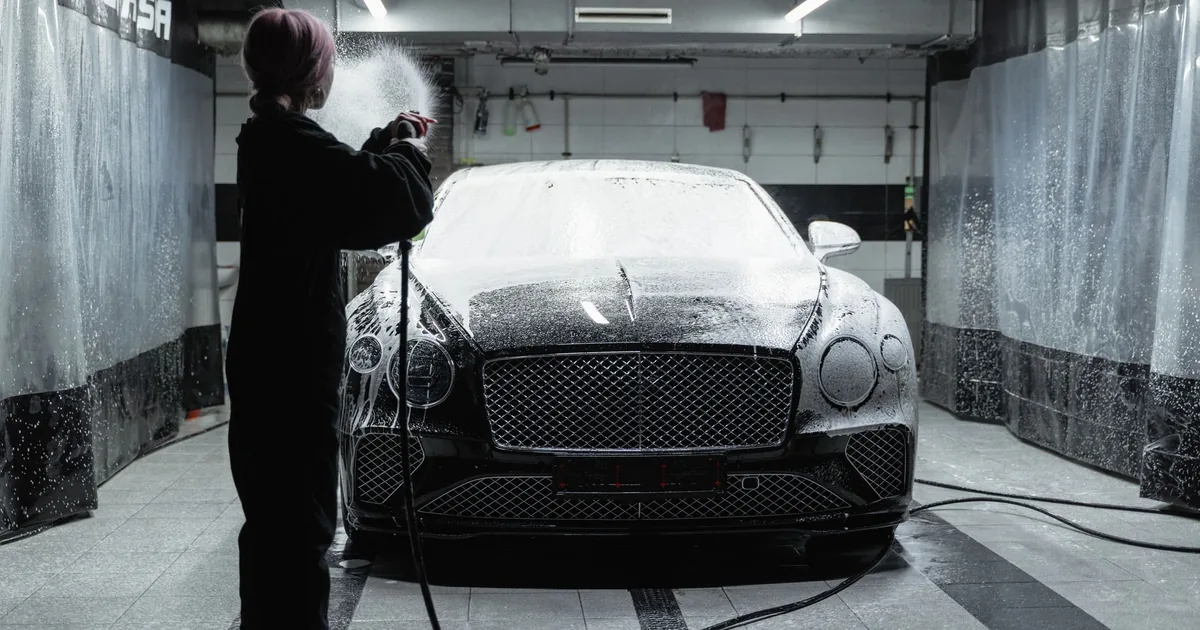 Person washing a car with foam in a garage setting.