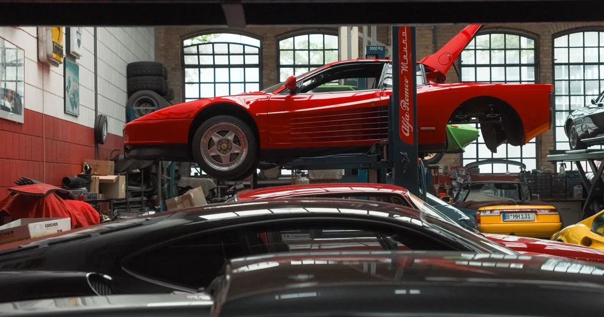 Red car on a lift in a garage with other cars parked below.