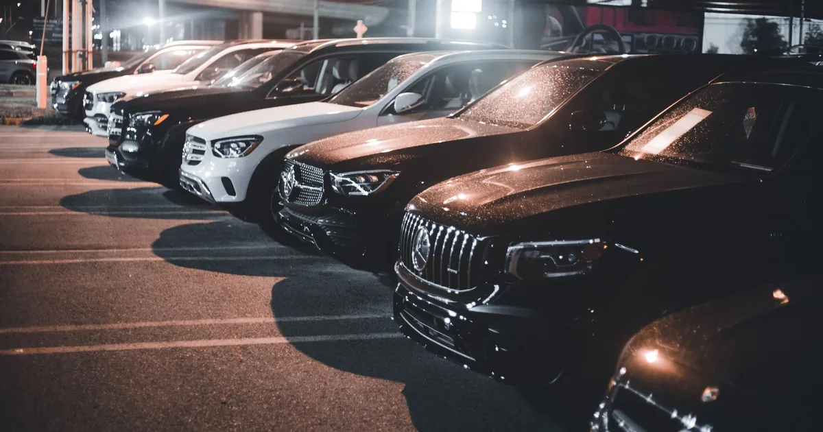 Row of various parked cars in a dimly lit parking lot at night.