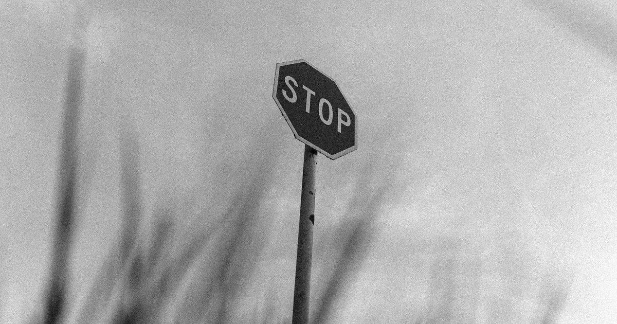 Stop sign stands tall in a parking area with grass in the foreground.