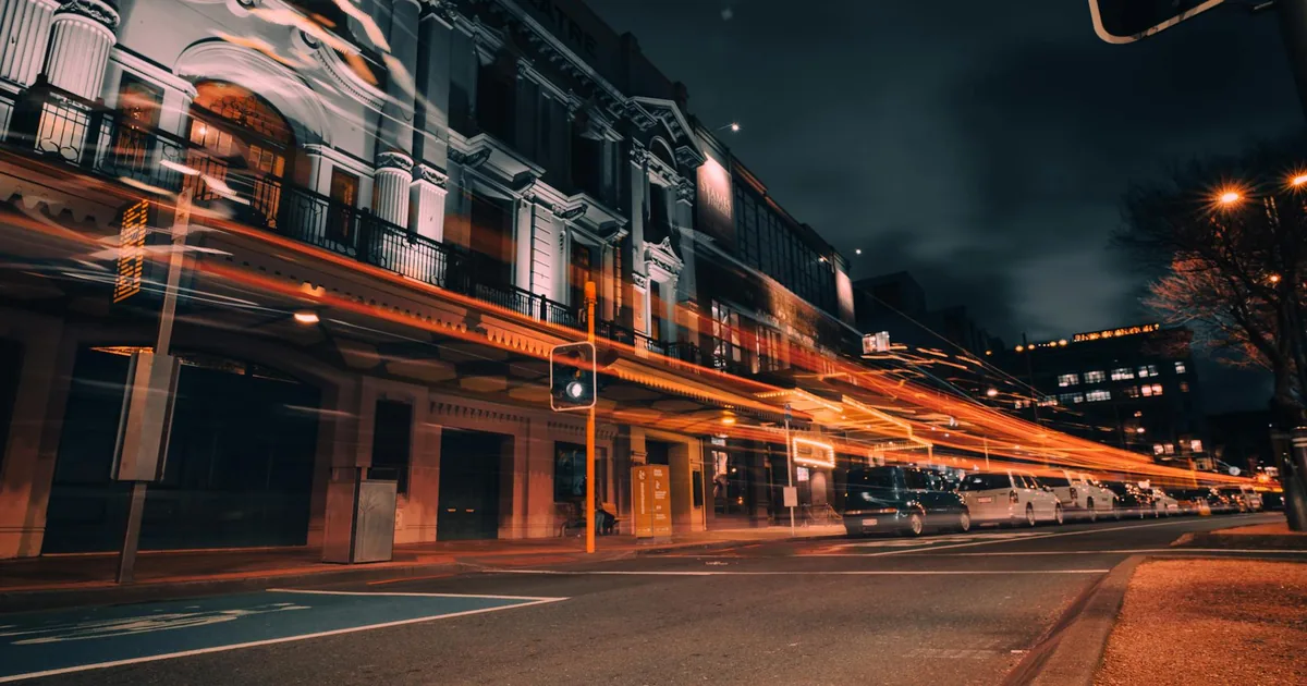 Street view at night with parked vehicles and light trails from.