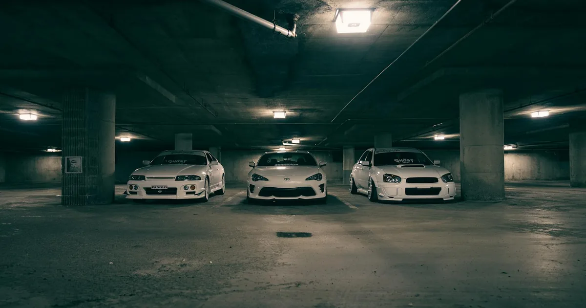 Three parked cars in an underground parking garage with dim lighting.