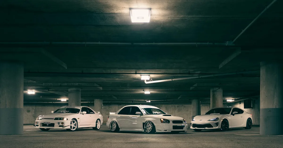 Three white cars parked in a dimly lit underground parking garage.