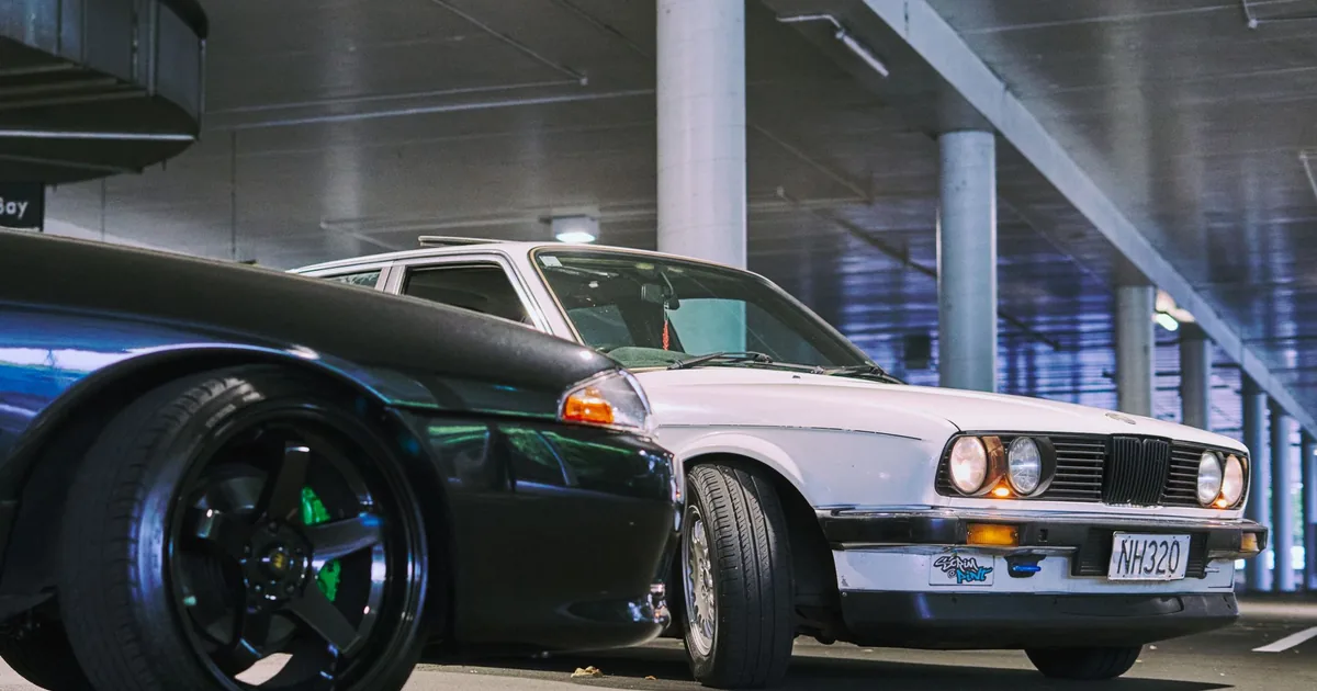 Two cars parked in a well lit indoor parking garage with concrete.