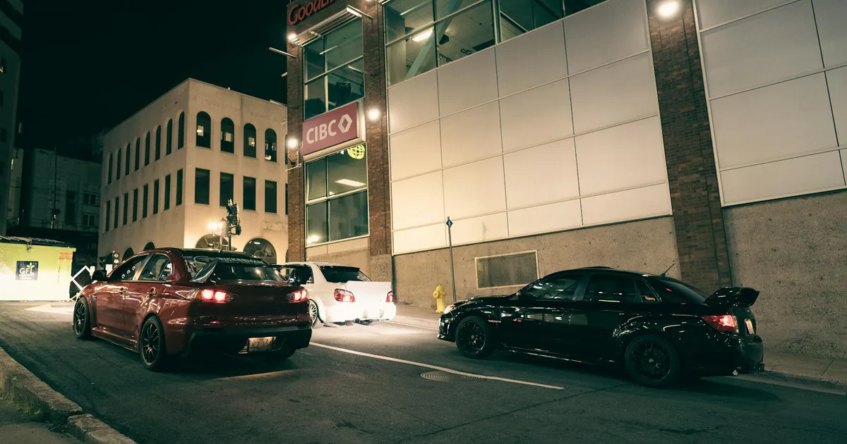 Two cars parked on a city street near a commercial building at night.