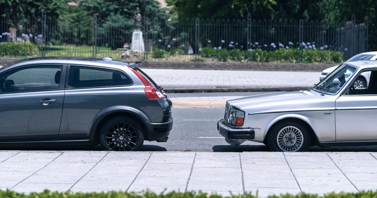 Two cars parked side by side on a city street with greenery in the.