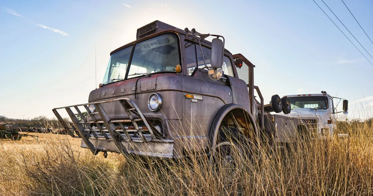 Two old trucks parked in a grassy field under a clear blue sky.