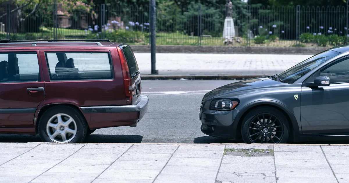 Two parked cars side by side on a city street with greenery in the.