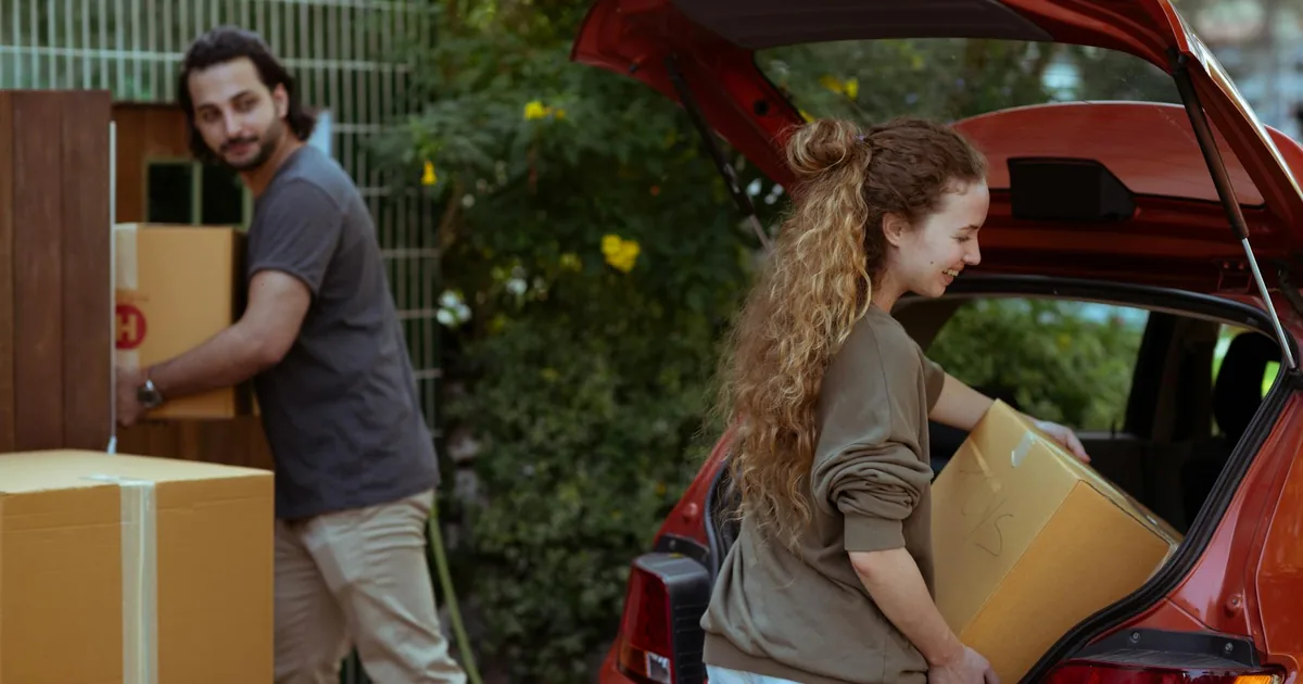 Two people unloading boxes from a parked car in a parking area.