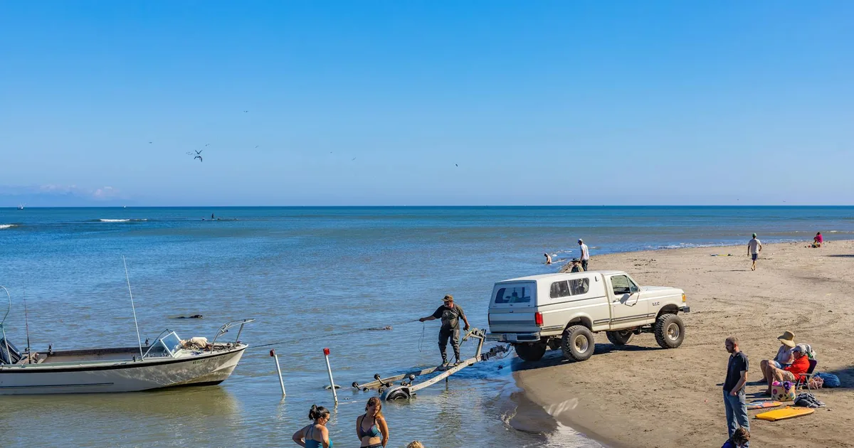 Vehicle parked near the beach with people enjoying the water and.