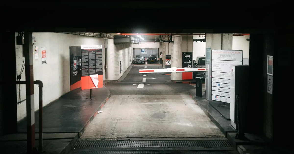 View of an underground parking entrance with barriers and signage.