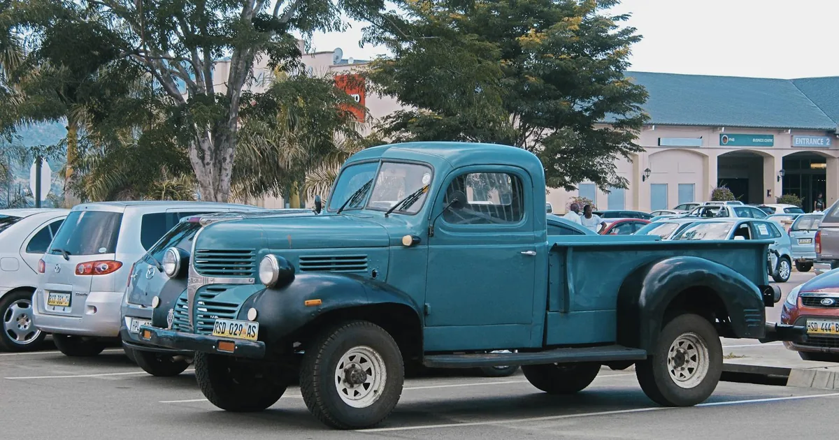 Vintage blue truck parked in a busy parking lot with other vehicles.