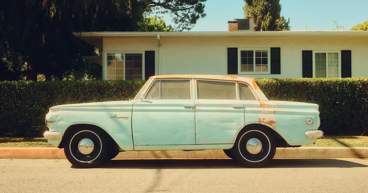 Vintage car parked along a residential street near a house.