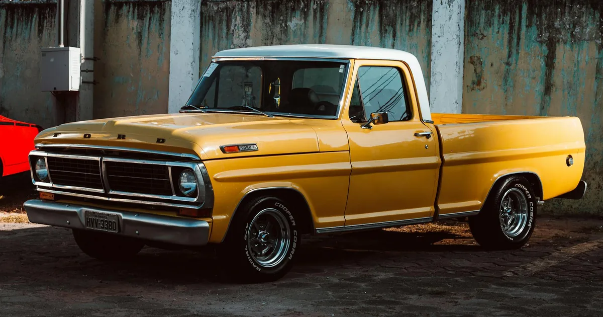 Vintage yellow pickup truck parked on a paved surface near a wall.