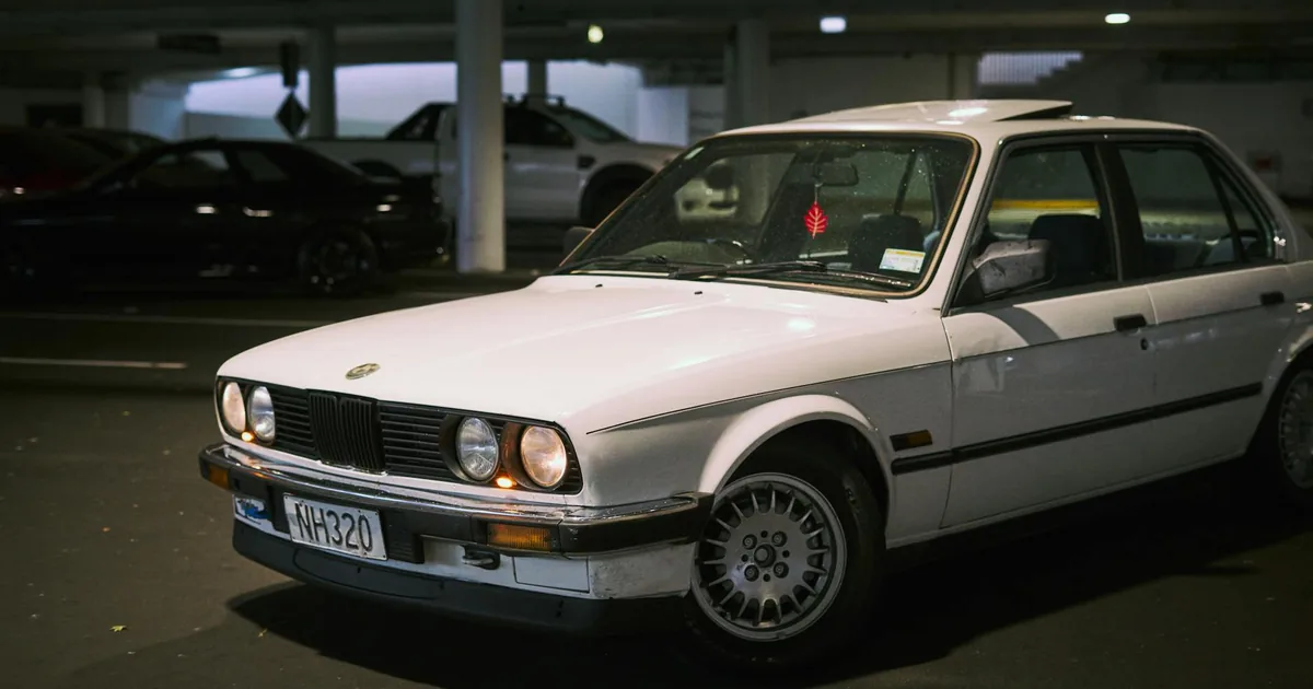 White car parked in a dimly lit parking garage with other cars.
