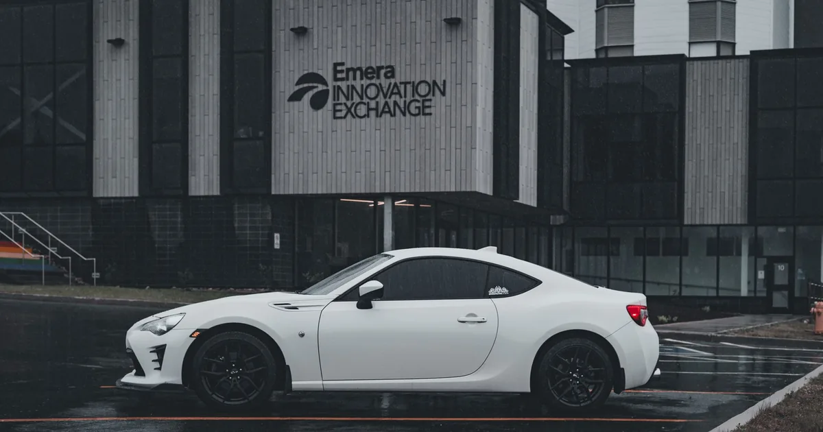 White car parked in front of a modern building on a rainy day.