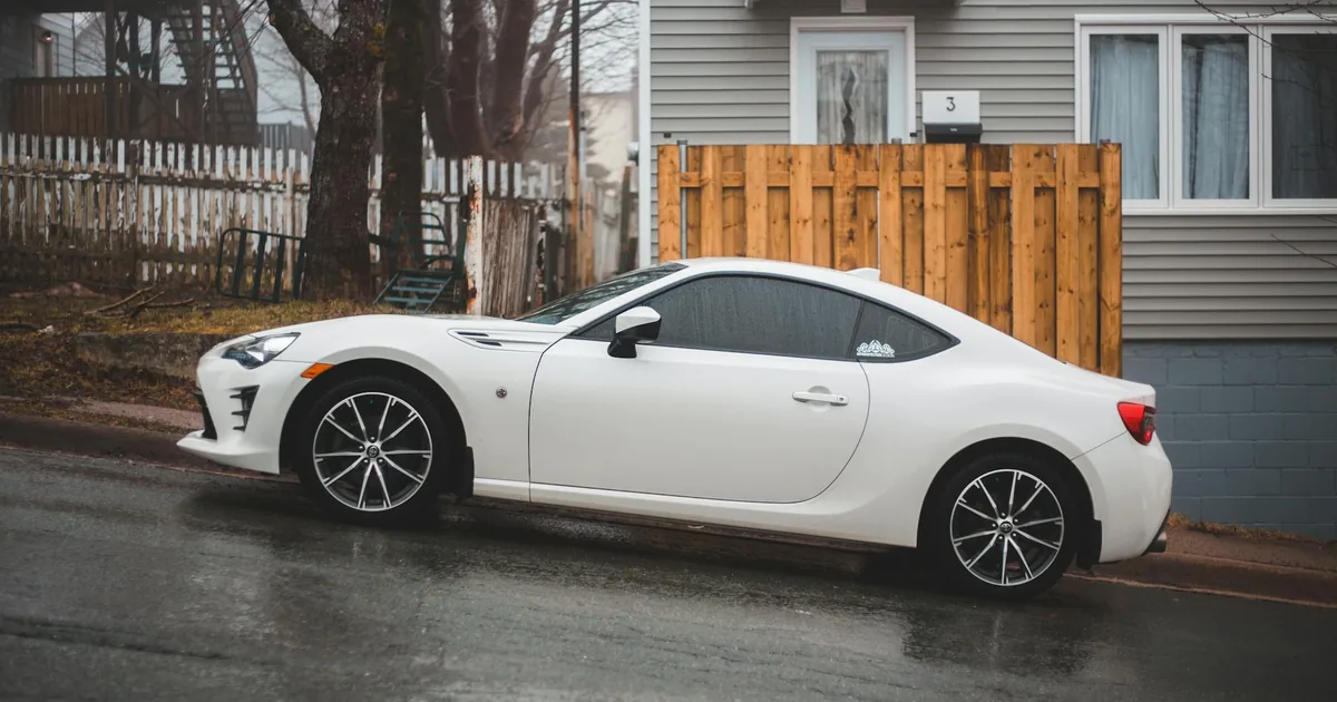 White car parked on a wet street beside a residential building.