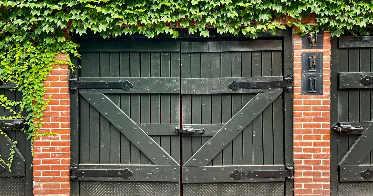 Wooden gate covered in ivy leading to a parking area behind a brick.