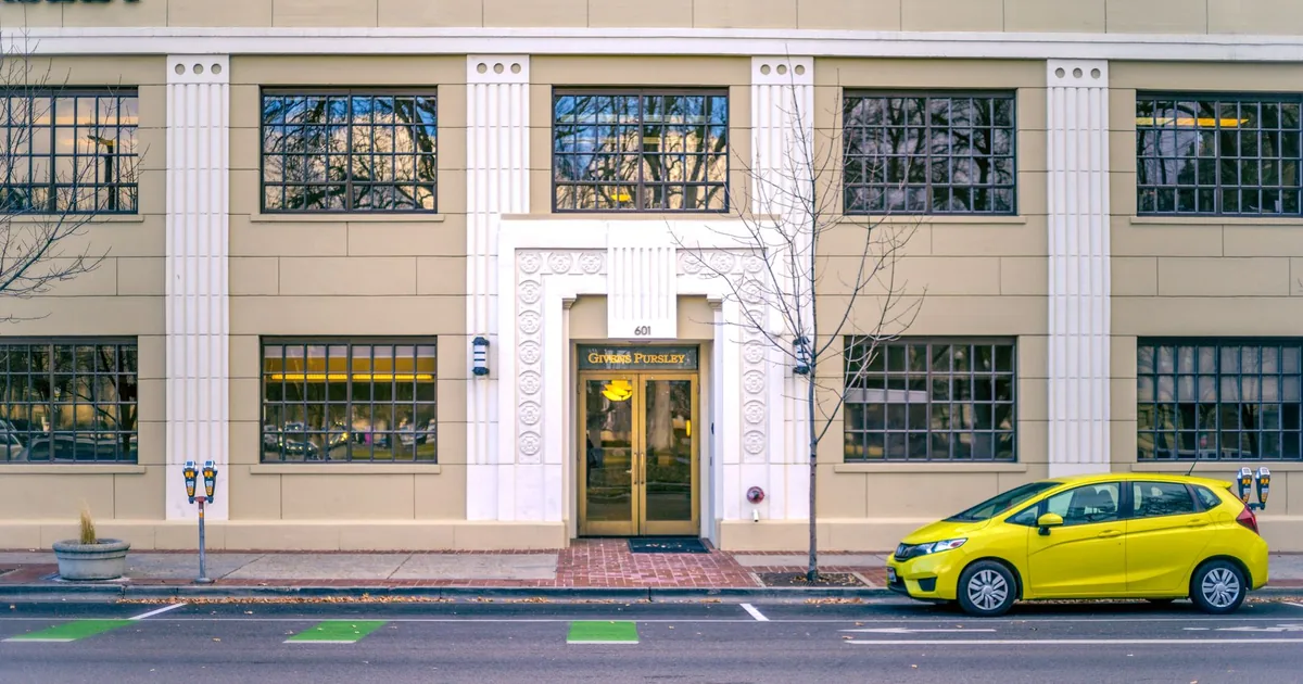 Yellow car parked on the street beside a building with large windows.