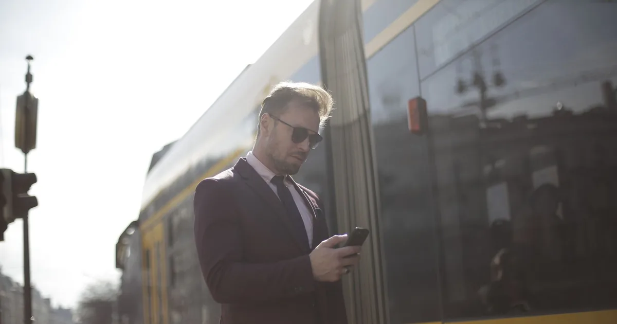A man in a suit checking his phone while waiting outdoors