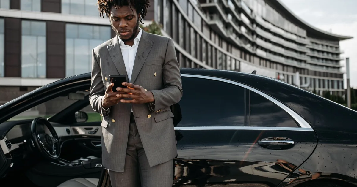 A man in a grey suit using his phone beside a car