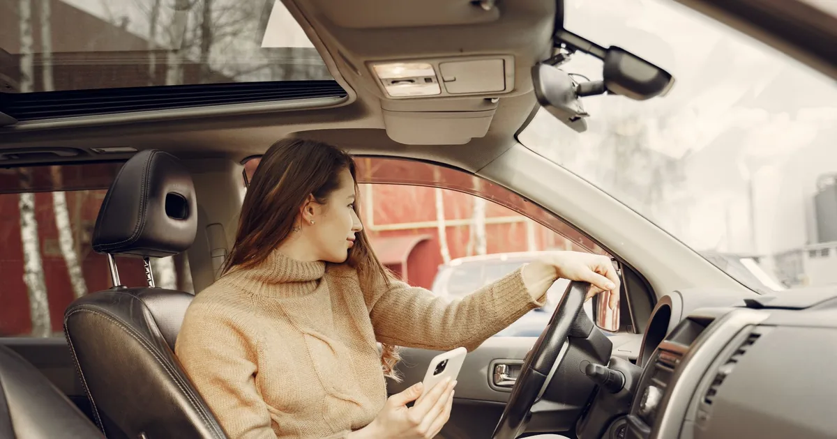 A woman sitting in the driver's seat of a car using her smartphone